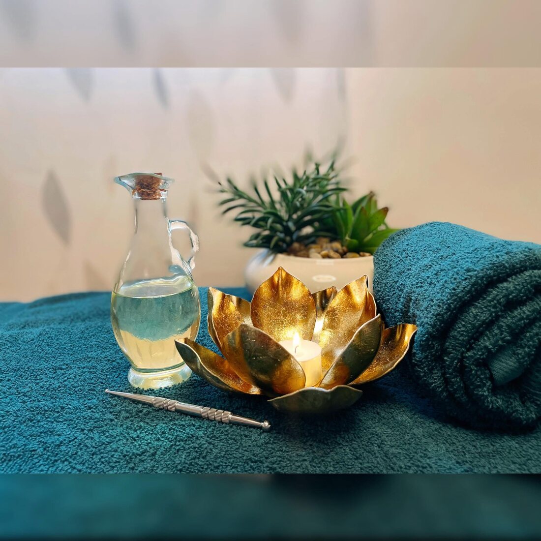 Massageöl und Lotusblüten-Kerze auf petrolfarbenen Handtüchern der Massageliege